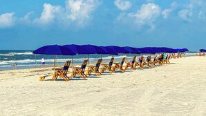 Une plage bordée de rangées de chaises longues en bois et de parasols bleus.