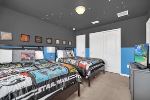 A bedroom with two beds, Star Wars themed bedding, a TV, and framed pictures on the wall.