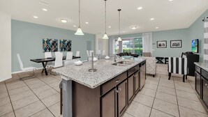 Una cocina moderna con encimeras de granito, una isla central y un comedor con sillas blancas.