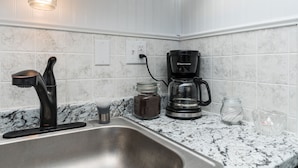A kitchen with a stainless steel sink, a coffee maker, and a jar of coffee. - Zen Den at Rockaway Rentals near Branson (Rockaway Beach)