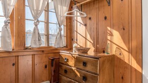 A wooden room with a dresser, a basket on top, and a hanging clothes rack. - Zen Den at Rockaway Rentals near Branson (Rockaway Beach)