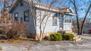 A single-story house with a gabled roof, a front porch, and a small front yard with a bush and a tree. - Zen Den at Rockaway Rentals near Branson (Rockaway Beach)