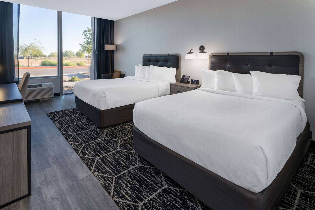 Une chambre d’hôtel avec deux lits, un bureau et une grande fenêtre donnant sur l’extérieur.