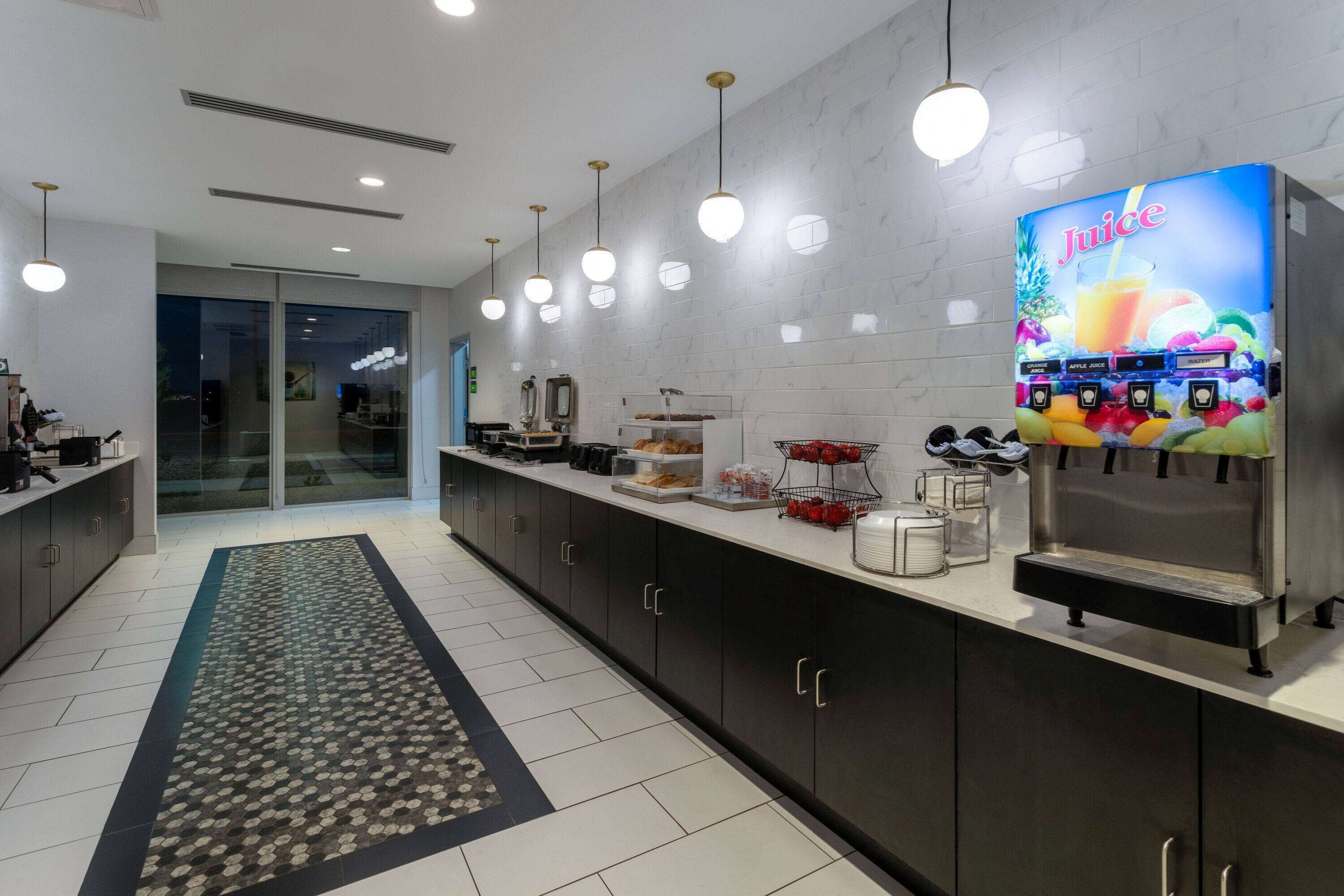 A modern kitchen with a juice dispenser, a coffee machine, and a refrigerator.