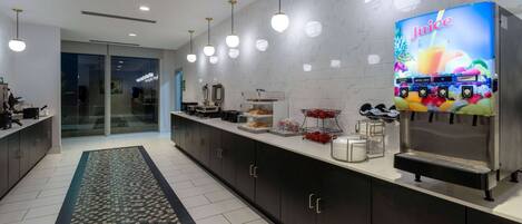 A modern kitchen with a juice dispenser, a coffee machine, and a refrigerator.