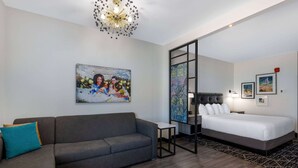 Une chambre d’hôtel moderne avec un canapé gris, un lit, une petite table et un élément décoratif mural.