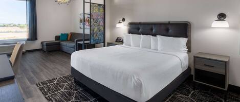 Una habitación de hotel moderna con una cama grande, un escritorio, una silla, un sofá y vistas al exterior.