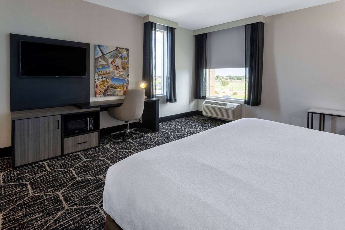 Une chambre d’hôtel dotée d’un grand lit, d’un téléviseur à écran plat, d’un bureau avec une chaise, d’un climatiseur fixé au mur et d’une fenêtre avec des rideaux.