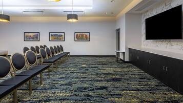 A conference room with rows of chairs, a large flat-screen TV, artwork on the wall, and a patterned carpet.