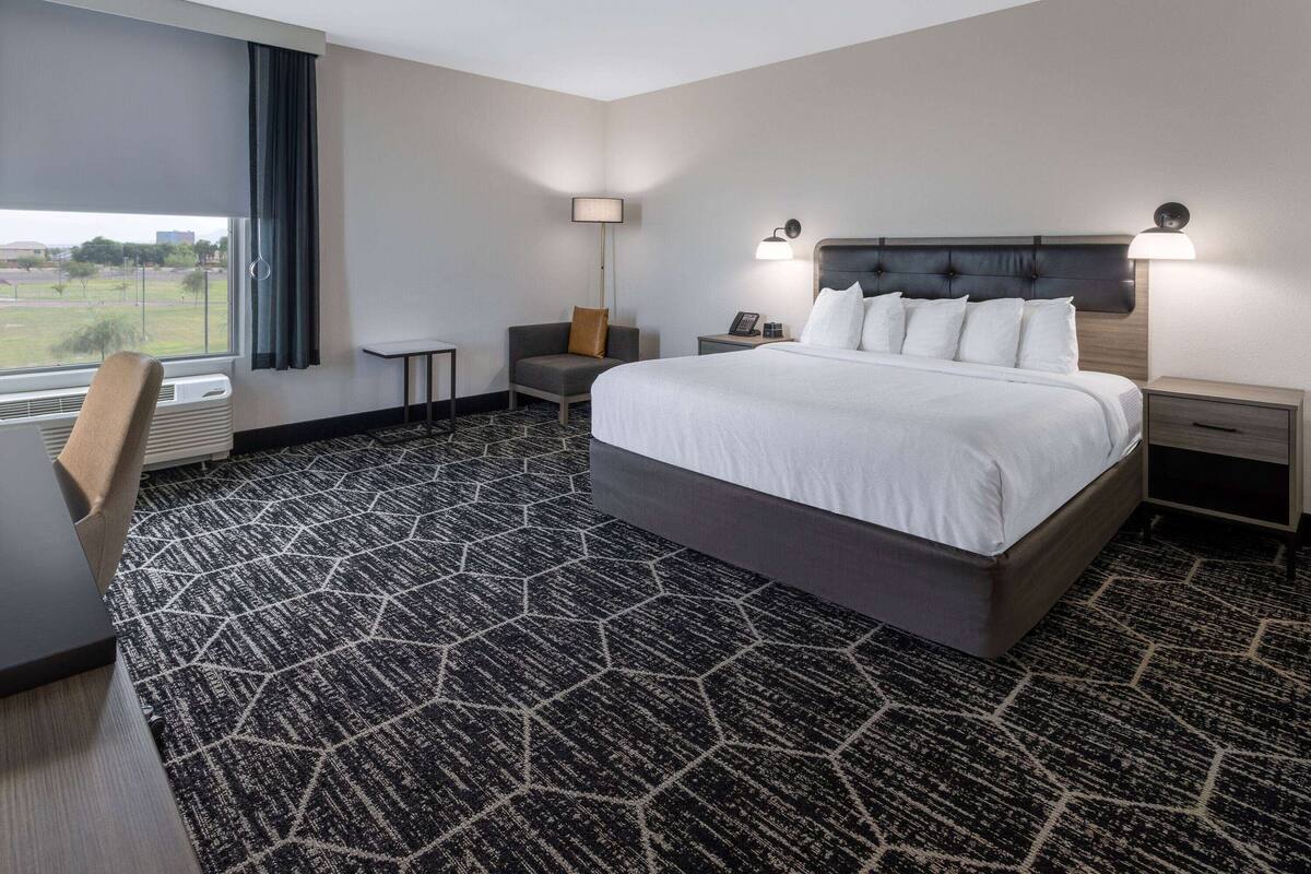 Une chambre d’hôtel avec un grand lit, un bureau, une chaise, une lampe et une vue sur l’extérieur.