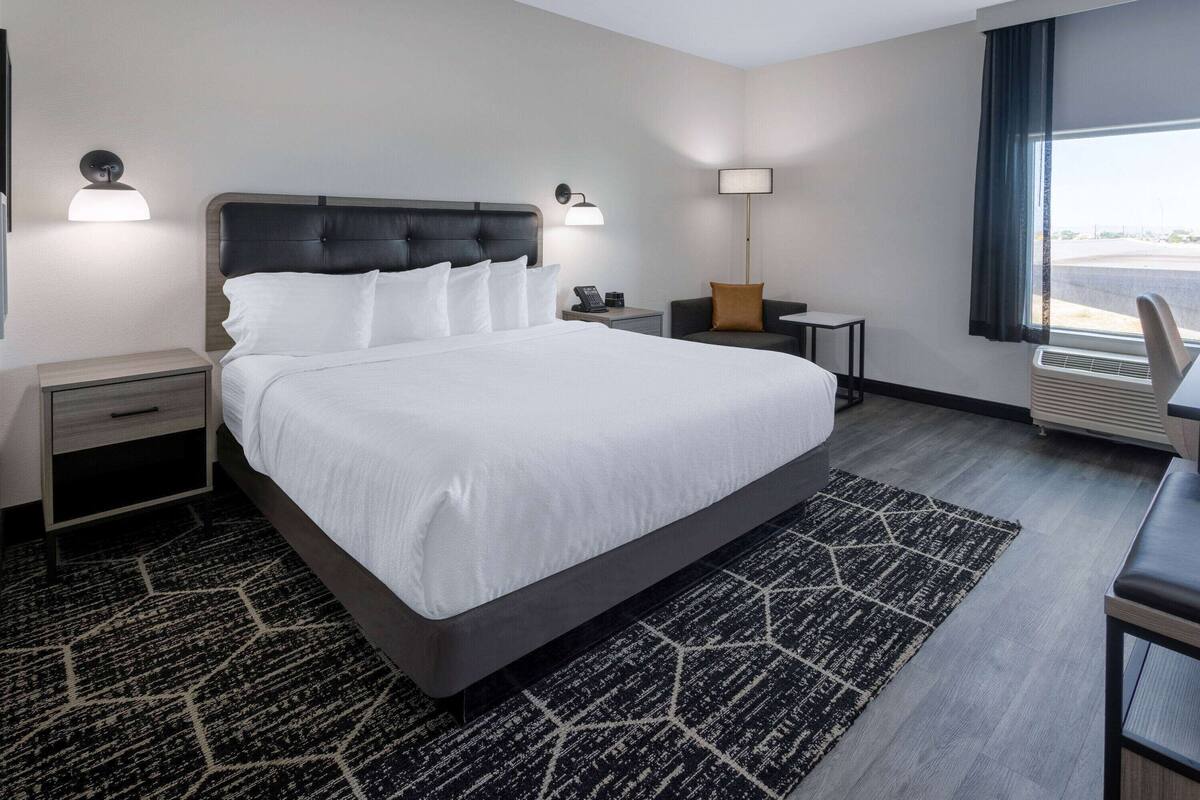 Une chambre d’hôtel moderne avec un grand lit, des tables de chevet, un bureau et une fenêtre donnant sur un beau paysage.