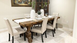 Ein Esszimmer mit einem rustikalen Holztisch, weißen Stühlen und einem Gemälde an der Wand.