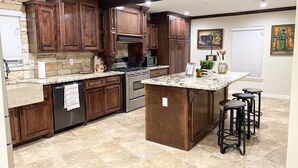 Eine Küche mit dunklen Holdschränken, einer Granitabdeckung, einem eingebauten Backofen und einer Bar mit Hockern.