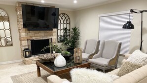 Ein Wohnzimmer mit Kamin aus Naturstein, einem Flachbildfernseher, zwei Sesseln, einem Sofa und einem Couchtisch mit Dekoration.