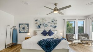 A bedroom with a bed, a ceiling fan, artwork on the wall, a chair, and a view of the outdoors. - Pvt Oasis Pickleball/Basketball/BBQ/Game Room/Pool (Bermuda Dunes)