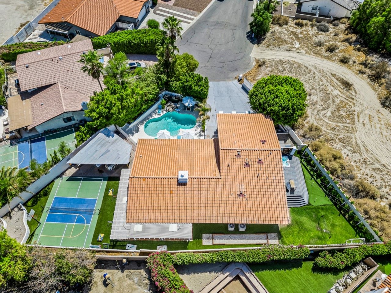 An aerial view of a residential property with a swimming pool, tennis courts, and a covered patio area.