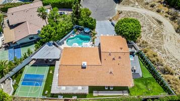 An aerial view of a residential property with a swimming pool, tennis courts, and a covered patio area.