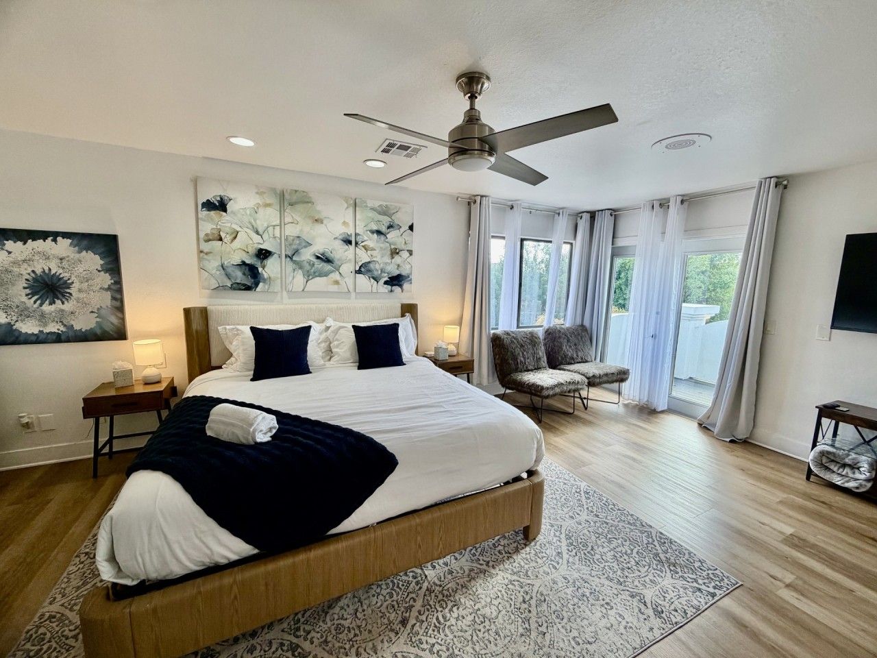 A modern bedroom with a large bed, a ceiling fan, and a view of the outdoors.