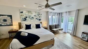A modern bedroom with a large bed, a ceiling fan, and a view of the outdoors.