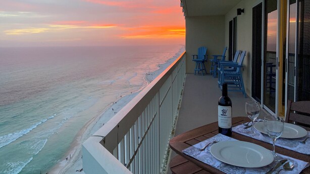 A balcony with a table set for two, overlooking a beach with a sunset view. - Waterfront High-Rise PCB Condo w/ Community Perks (Panama City Beach)