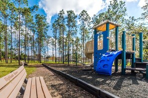 Un terrain de jeux équipé d’un toboggan et de structures d’escalade, entouré d’une zone boisée.