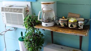 Uma cozinha com cafeteira, uma prateleira com canecas vermelhas e um ar condicionado.