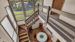 A modern interior with a staircase connecting two levels, a round table with chairs, and large windows with blinds. - Outlook 1 - Unit 1 Narira St 9 (BERMAGUI)