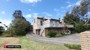 A two-story house with a balcony, surrounded by trees and a paved driveway. - Outlook 1 - Unit 1 Narira St 9 (BERMAGUI)