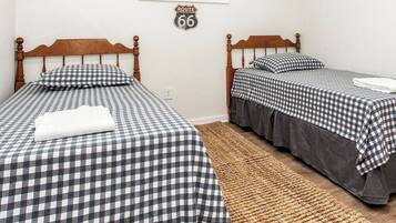 Una habitación con dos camas de madera, cada una con colcha a cuadros y almohadas a juego. Un tapiz tejido cubre el suelo, y un cartel de 'Route 66' está en la pared.