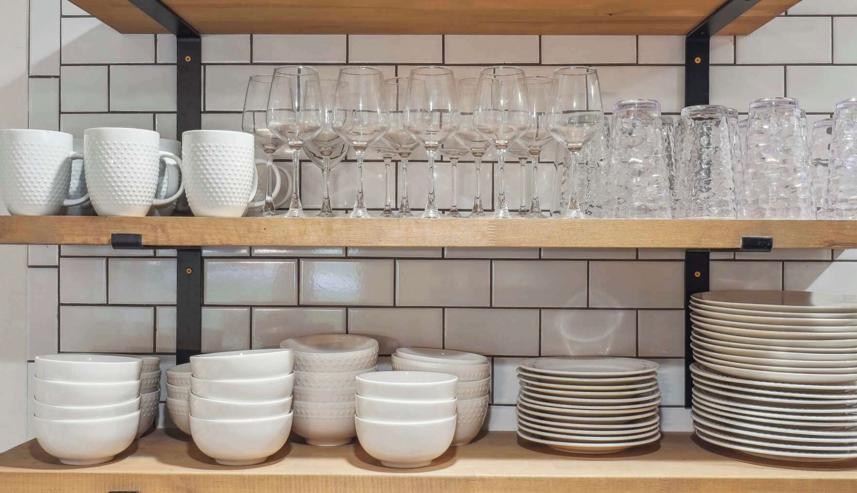 A kitchen shelf with various glassware and white ceramic dishes.