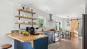 A modern kitchen with a central island, wooden shelves, and a coffee sign. - The Gathering Grove (Tucker)