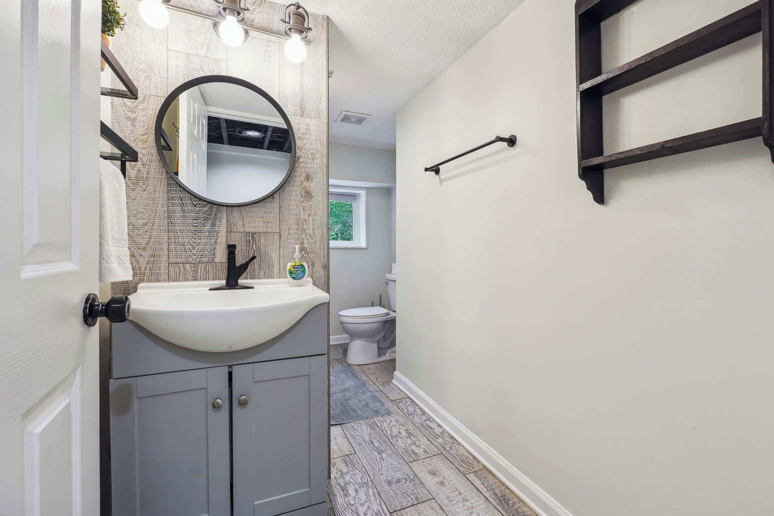 A bathroom with a white sink, a round mirror, and a towel rack.