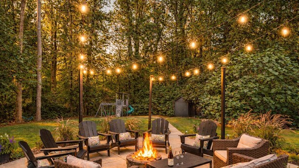 An outdoor patio with wicker furniture, a fire pit, and string lights. - The Gathering Grove (Tucker)