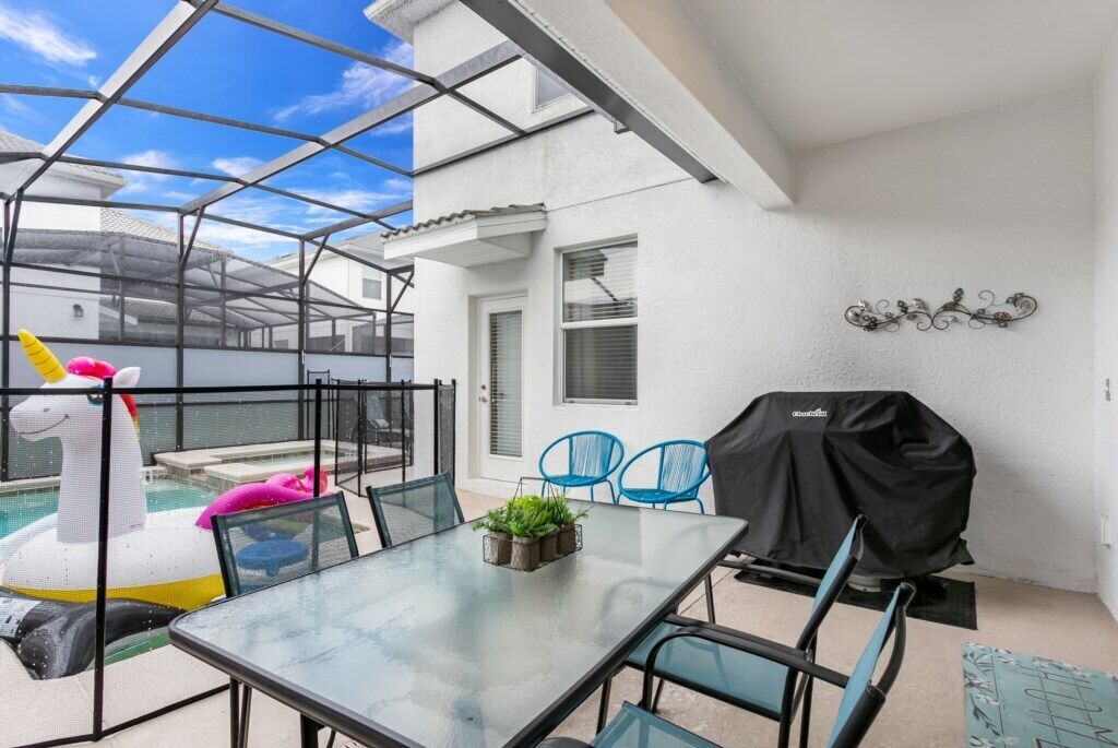 A glass-enclosed patio with a pool, a table with chairs, a grill, and a decorative wall piece.