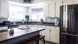 A modern kitchen with white cabinets, a stainless steel refrigerator, a wooden island, and a coffee maker.