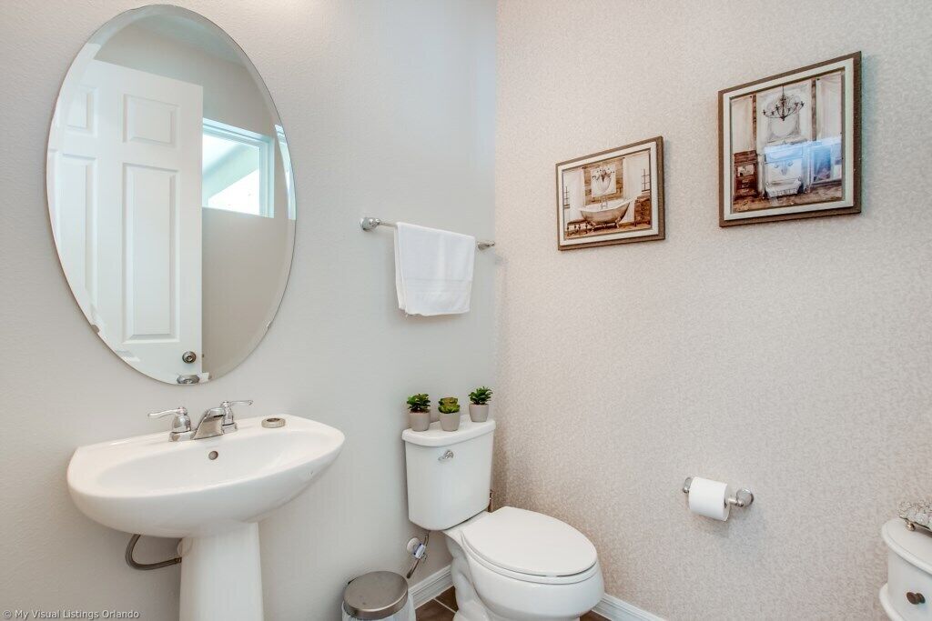 Un baño con lavamanos, inodoro y espejo blancos. Hay dos cuadros enmarcados en la pared.