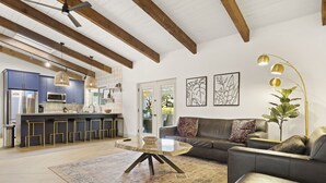 Et moderne køkken med indbygget mikrobølgeovn og køleskab i rustfrit stål, et spiseområde med et rundt bord og stole, en stue med sofa og sofabord, samt en loftventilator.
