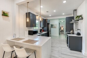 A modern kitchen with white marble countertops, dark cabinetry, and pendant lighting.