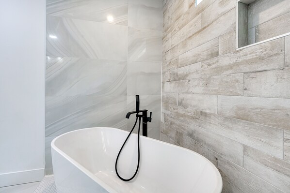 A modern bathroom with a freestanding bathtub, a showerhead, and a wooden wall panel.
