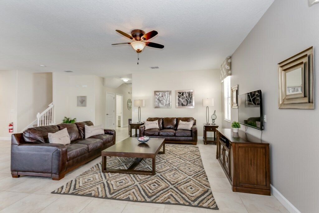 A spacious living room with a ceiling fan, a brown leather sofa, a coffee table, and a patterned rug.