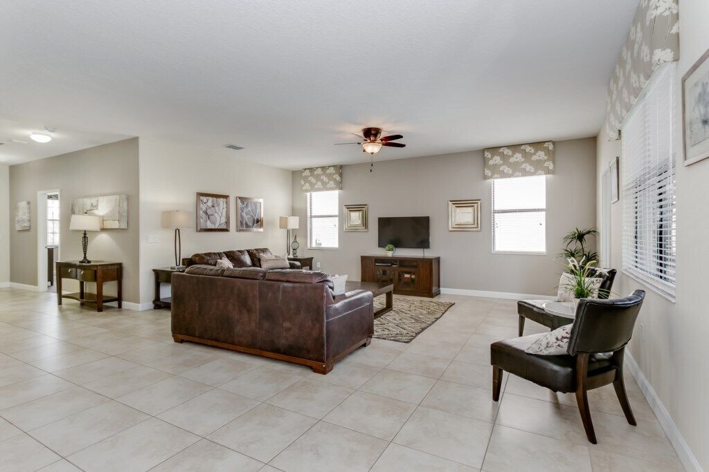 A spacious living room with a brown leather sofa, a dining table with chairs, a TV, and a ceiling fan.