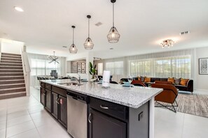 A modern kitchen with granite countertops, a dishwasher, and a large island. There is a dining area with a sofa and a coffee table.