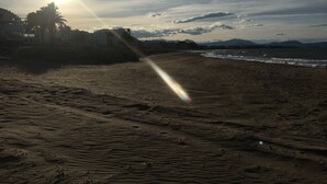 Une plage où l’on peut voir le soleil, le sable et des montagnes au loin.