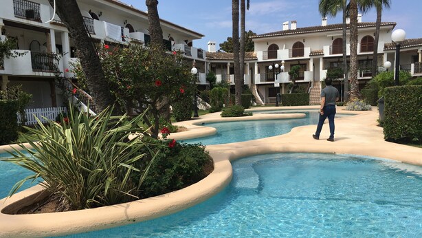 Une piscine au design incurvé, entourée de palmiers et bordée d’un bâtiment doté de balcons.