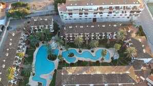 Vue aérienne d’un complexe hôtelier doté de plusieurs piscines, de palmiers et d’un grand bâtiment avec des balcons.