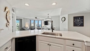 A modern kitchen with a large island, white cabinetry, and a view to the living area.
