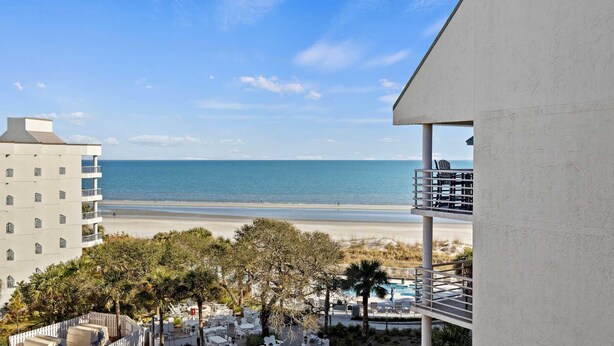 A beachfront hotel with a pool, outdoor seating, and a view of the ocean.