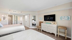 A bedroom with two beds, a dresser, a television, and artwork on the walls.