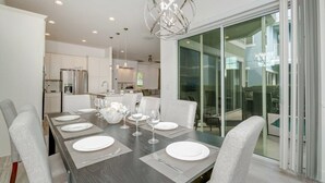 A modern dining area with a dark wooden table set for six, white chairs, and a unique spherical chandelier. - New Listing! Reunion Resort, 6mi to Disney & 16mi to Universal - FS321450 (Kissimmee)
