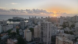 A cityscape with high-rise buildings, a body of water, and a sunset. - San Juan Sunrise - Apex Living in the Capital of Puerto Rico (San Juan)